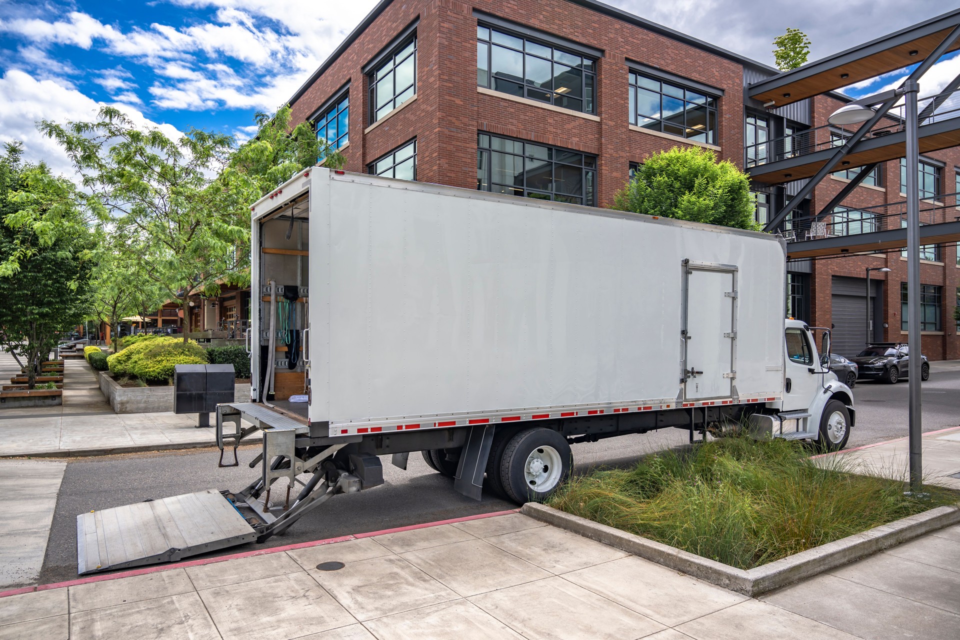 Middle duty day cab moving rig semi truck with long box trailer and lift on the back standing on the urban street delivering goods to new apartment